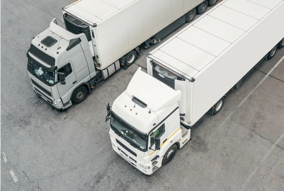 Two large freight trucks parked in an industrial area, showcasing the logistics and transportation capability of the company.